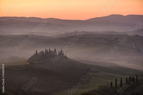 Podere belvedere house on a hills in tuscany in italy at sunrise with beautiful light and myst and fog on sweet hills with cypresses trees