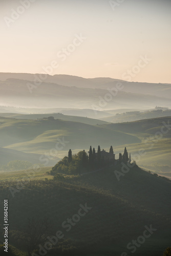 Podere belvedere house on a hills in tuscany in italy at sunrise with beautiful light and myst and fog on sweet hills with cypresses trees