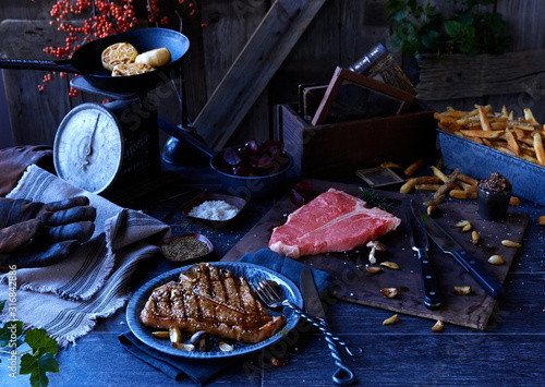 Farmhouse kitchen scene with grilled and raw tbone steaks, fries, roasted garlic, salt and pepper photo