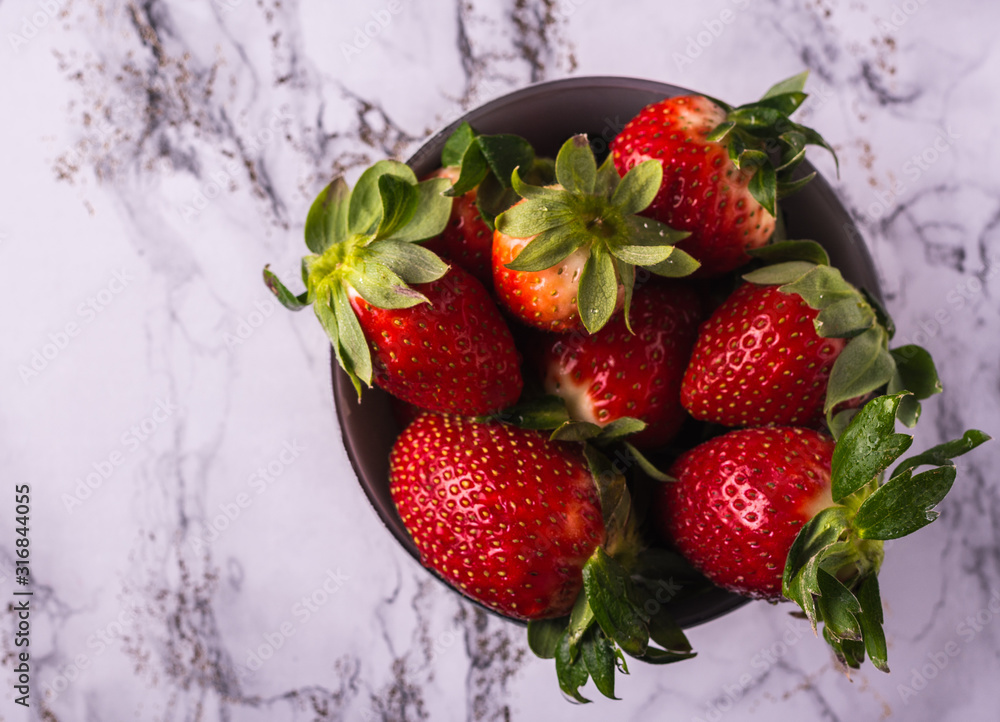 Delicious red strawberries with green leaves in a gray bowl. White marble background. Hotizontal format. Delicious red strawberries with green leaves in a gray bowl. White marble background. Hotizontal format.