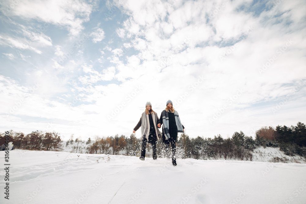 Cute girls walking in a winter park. Sisters have fun with snow. Ladies in a cute hats