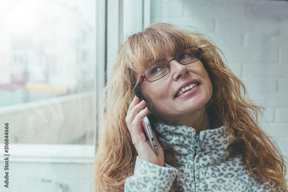 adult or senior woman talking on mobile phone at home in the window adult or senior woman talking on mobile phone at home in the window