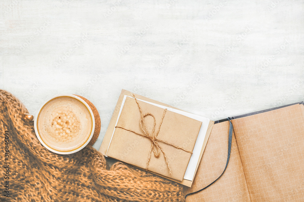 Coffee cup with beige brown knitted scarf and correspondence notebook on vintage white wooden background with space. Top view. Flat lay Coffee cup with beige brown knitted scarf and correspondence notebook on vintage white wooden background with space. Top view. Flat lay