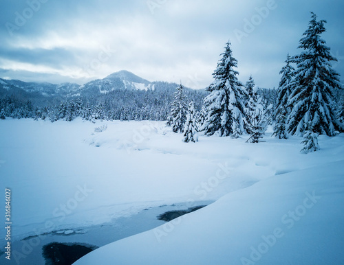Snow covered frozen beautiful Gold Creek Pond with snow covered trees and trail during the winter in the Alpine Lakes Wilderness in Kittitas county Washington State