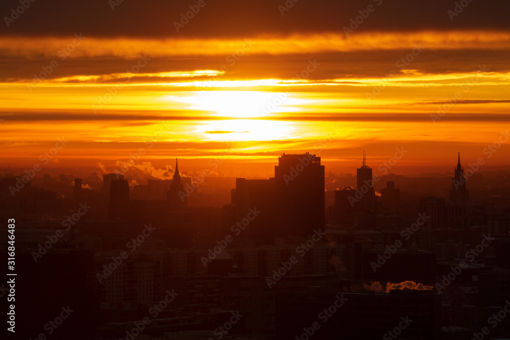 Sunrise over the city. Aerial view of Moscow, silhouettes of buildings in downtown with colorful lighting sunrise sky and soft clouds. Factories pipe, of which there are smoke. Rising sun