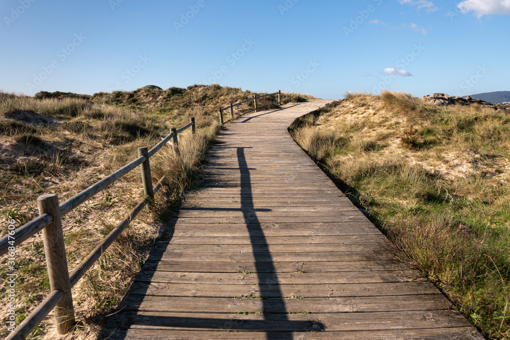 Landscape with a wooden walk way crossing a wild beach with sand and vegetation. Illa de Arousa, Pontevedra, Spain