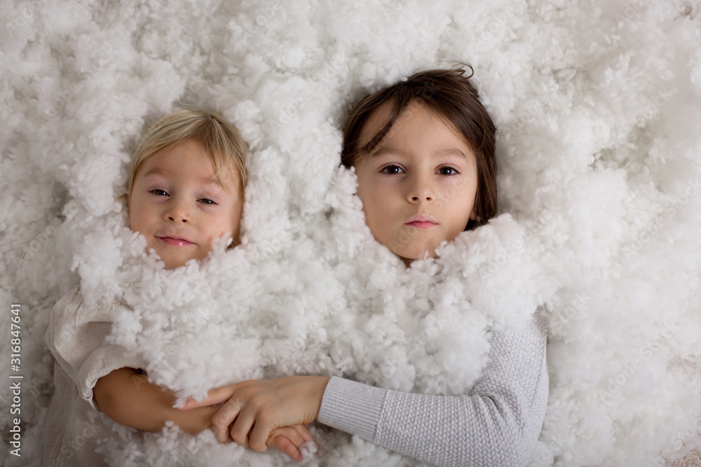 Beautiful portrait of three sibling boys, lying on the floor in a pile of cotton, holding hands, looking at camera Beautiful portrait of three sibling boys, lying on the floor in a pile of cotton, holding hands, looking at camera