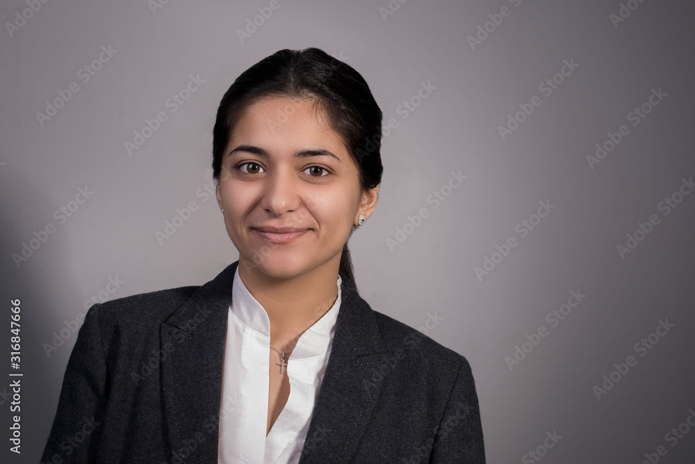 Portrait of thirty beautiful young business lady, in a business suit, holding her arms crossed on her chest, smiling. On a gray background, studio photography. Business concept Portrait of thirty beautiful young business lady, in a business suit, holding her arms crossed on her chest, smiling. On a gray background, studio photography. Business concept