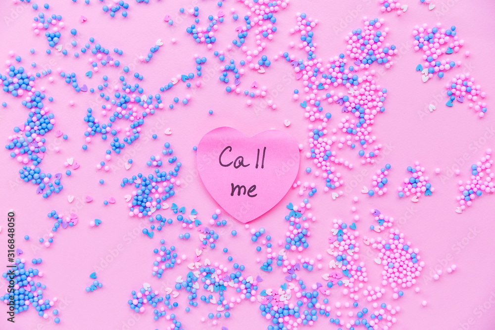 Paper pink heart on a background of decorative balls in blue and pink. There is a text on  heart call me