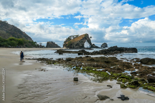 Woman walking on an idyllic Koka Beach. Hidden gem of Flores Indonesia. She is enjoying a solo escape. Waves gently washing the shore. Lots of stones on the beach. Happiness, adventure and discovering