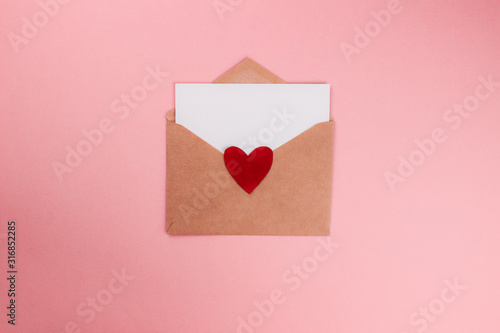 Love letter with white paper sheet in craft paper envelope with red heart flat lay on colorful pink background. 8 march, Mother's day, Valentine's Day template. Top view with copy space. Stock photo