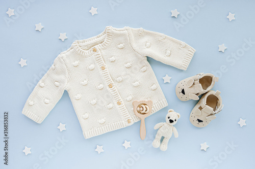 Pastel knitted jumper, toys and baby shoes. Cute set of baby clothes and accessories  blue background with stars.  Fashion newborn. Flat lay, top view photo