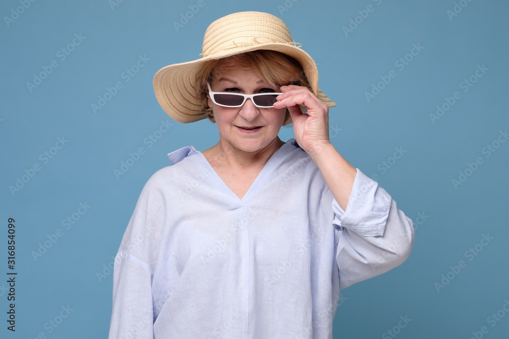 Elegant positive woman in summer hat and pink glasses holding smiling posing to the camera ready for vacation. Studio shot Elegant positive woman in summer hat and pink glasses holding smiling posing to the camera ready for vacation. Studio shot
