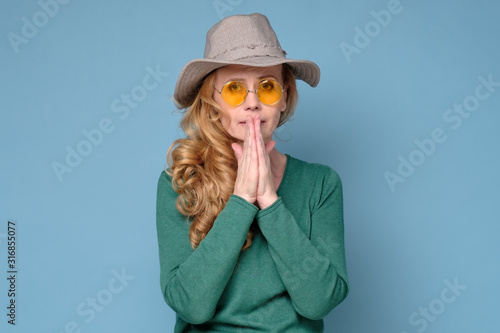 Beautiful woman keeps palms pressed together in front of her, has regretful or sorrorful expression, needs attention. Studio shot photo