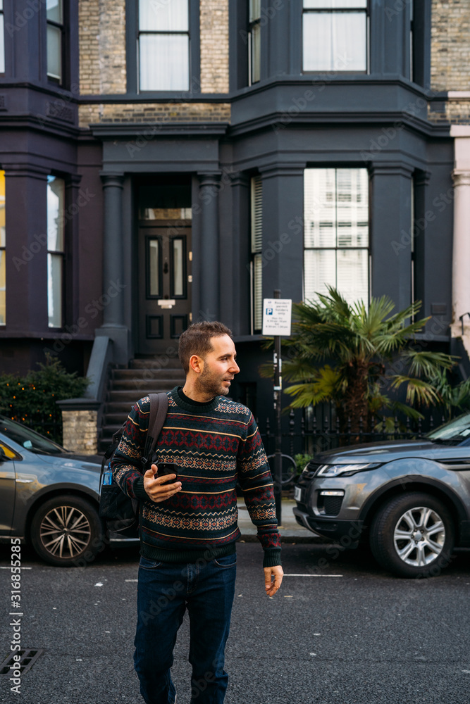 Fototapeta premium Young man leaving his house and using his smart mobile with colorful houses on Portobello Street in the Notting Hill neighborhood