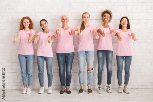 Happy Women In Awareness T-Shirts Gesturing Thumbs-Up Over White Wall
