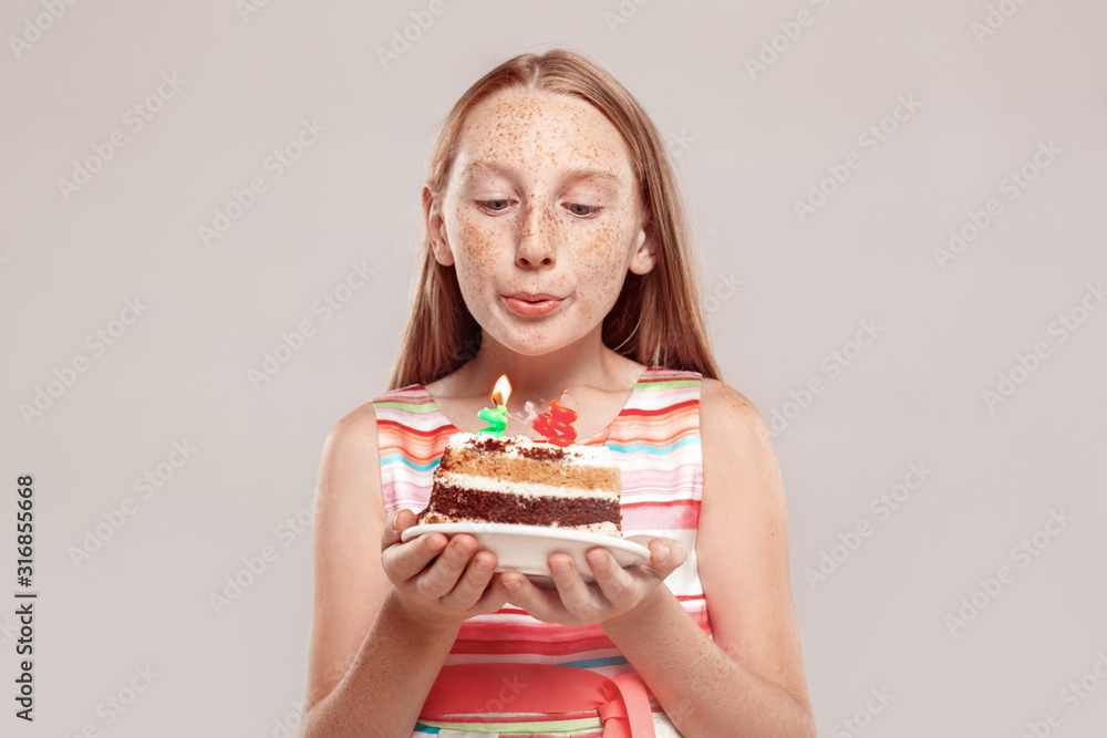 Inclusive Beauty. Girl with freckles standing isolated on grey holding birthday cake blowing candles making wish close-up
