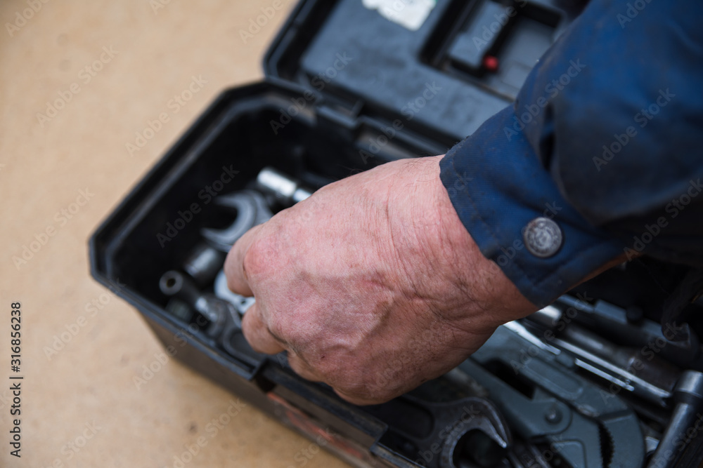 A male mechanic is sorting out wrenches in a box with tools for repair of faulty equipment. Hands smeared with grease are holding various wrenches. Workshop and repairing A male mechanic is sorting out wrenches in a box with tools for repair of faulty equipment. Hands smeared with grease are holding various wrenches. Workshop and repairing