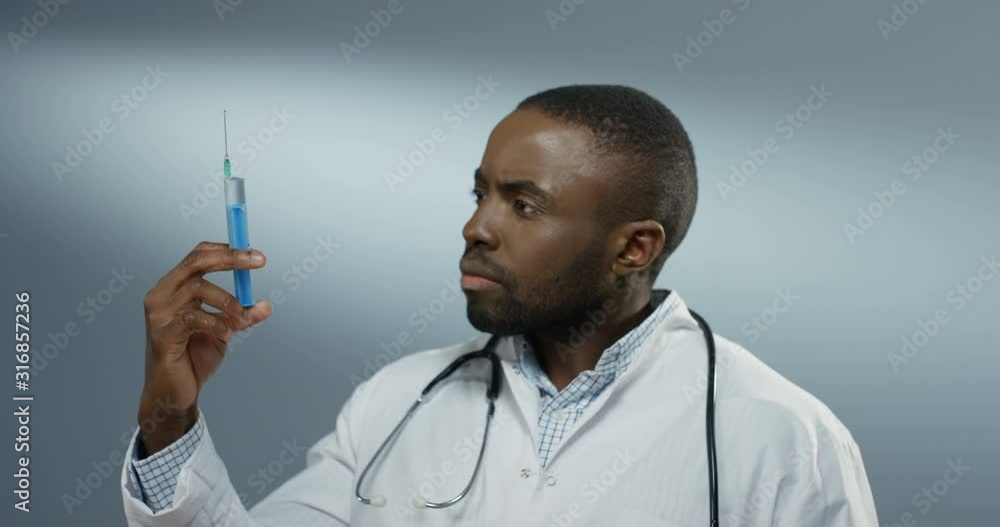African American good looking young male doctor or intern holding a syringe with a needle and withdrawing fluid from it. Close up. African American good looking young male doctor or intern holding a syringe with a needle and withdrawing fluid from it. Close up.