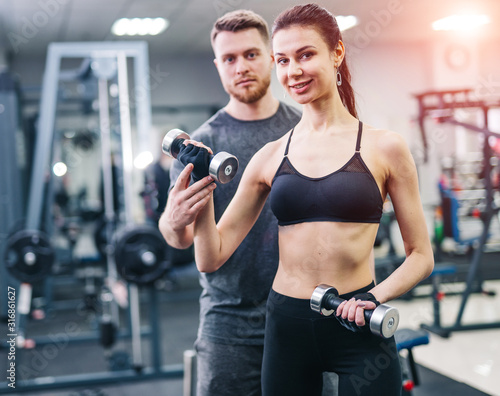 Personal trainer helping woman working with heavy dumbbells indoors. Beautiful female with her fitness trainer exercising in the gym.