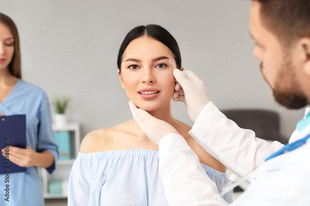 Plastic surgeon examining young woman's face prior to operation in clinic Plastic surgeon examining young woman's face prior to operation in clinic