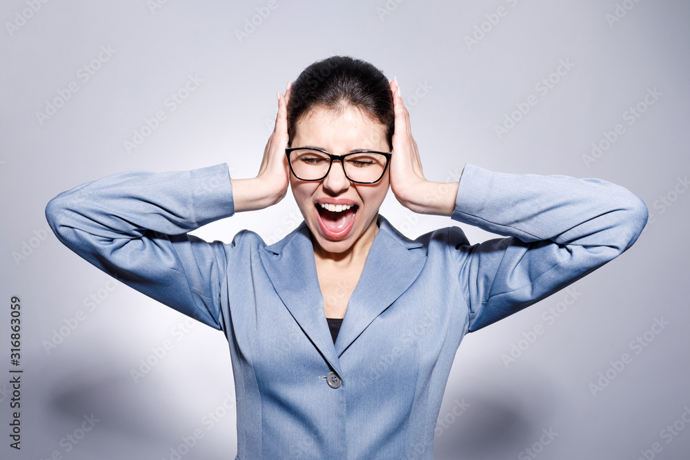 Annoyed female office clerk screaming with her eyes closed and hands closing ears isolated blue-gray background Annoyed female office clerk screaming with her eyes closed and hands closing ears isolated blue-gray background