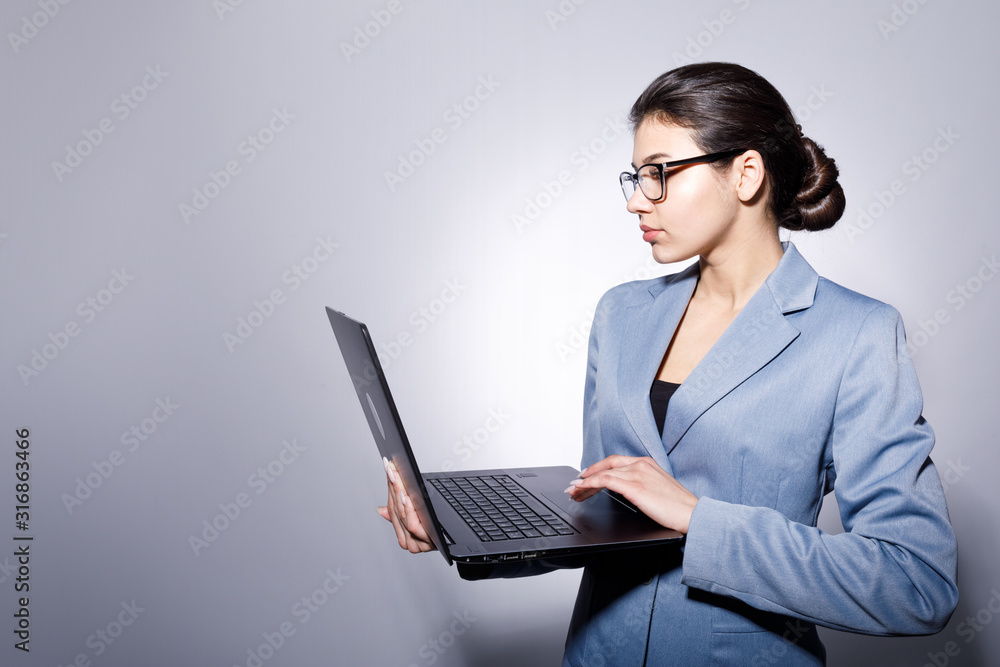Cute young office clerk standing and using laptop isolated blue-gray background copyspace Cute young office clerk standing and using laptop isolated blue-gray background copyspace