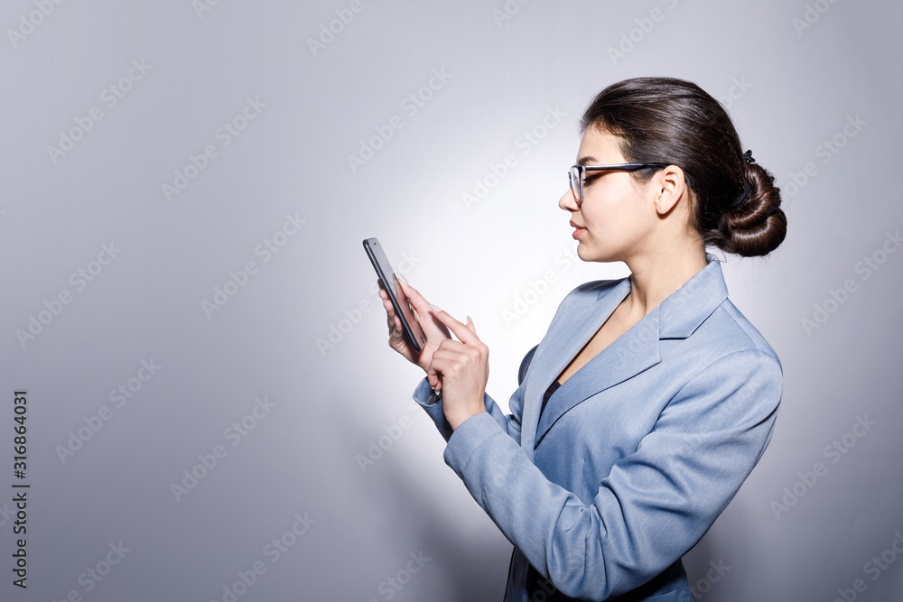 Sideview portrait of attractive young businesswoman in glasses using smartphone isolated blue-gray background copyspace Sideview portrait of attractive young businesswoman in glasses using smartphone isolated blue-gray background copyspace