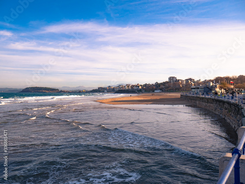 View of Sardinero beach and the promenade with the Magdalena palace in the background and a beautiful sky with clouds at sunset