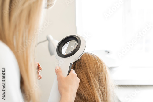 A trichologist examines the condition of the hair on the patient head with a dermatoscope. In a bright cosmetology room photo