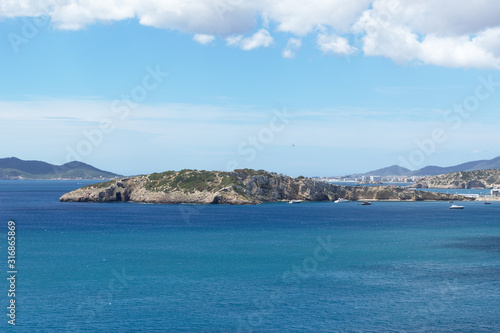 Rocky sea coast with clean blue water  cloudy sky and city view. Ibiza island  Spain