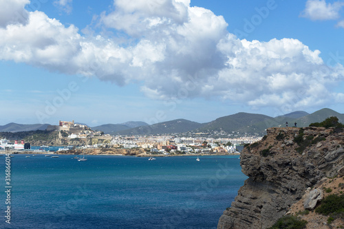 Fototapeta Naklejka Na Ścianę i Meble -  Rocky sea coast with clean blue water, cloudy sky and city view. Ibiza island, Spain