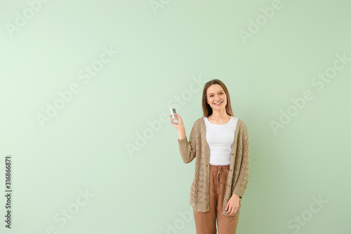 Young woman with air conditioner remote control on color background