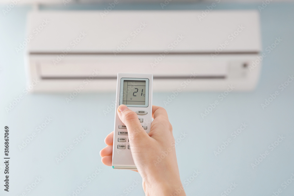 Young woman switching on air conditioner at home Young woman switching on air conditioner at home