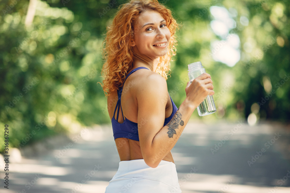 Girl training. Woman in a sports shorts. Redheads girl in a summer park