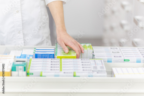 Pharmacist holding medicine box and capsule pack in pharmacy drugstore.
