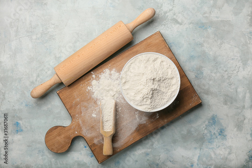 Flour with rolling pin and board on color background