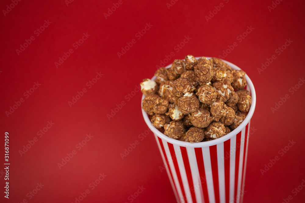 Butter popcorn chocolate in a red popcorn cup, snack in the house or cinema on a red background