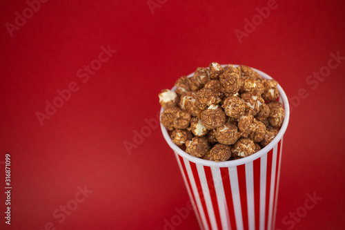 Butter popcorn chocolate in a red popcorn cup, snack in the house or cinema on a red background