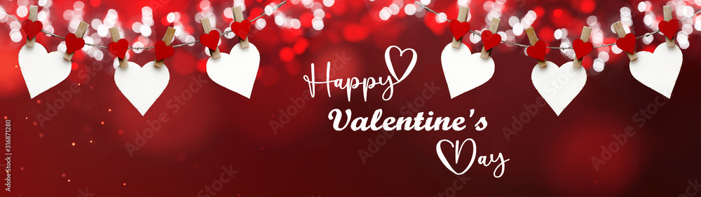 Naklejka premium Happy Valentine's Day background banner panorama - White heart hang on wooden clothes pegs with wooden heart and bokeh lights on a string isolated on red texture with bokeh lights, with space for text