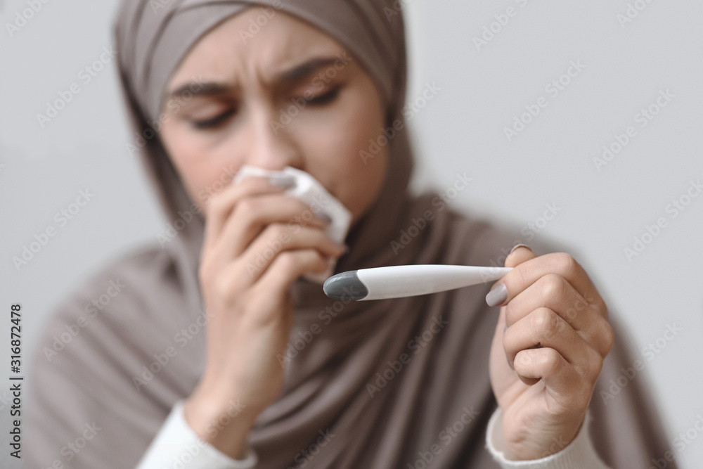 Sick arabic woman in headscarf holding thermometer and blowing runny nose Sick arabic woman in headscarf holding thermometer and blowing runny nose