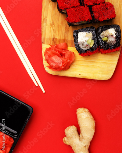 Rolls on a wooden board, sauce, wassabi and ginger on a red background. A look from above. photo