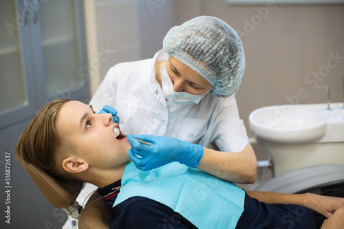 Dentist doing teeth checkup of guy in a dental chair at stomatology clinic.