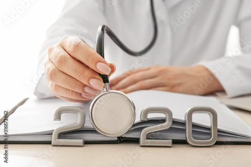 Female doctor with stethoscope, notebook and figure 2020 on table, closeup