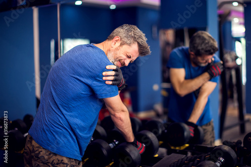 Tablou pe pânză Man feeling strong shoulder pain while training with dumbbells in the gym