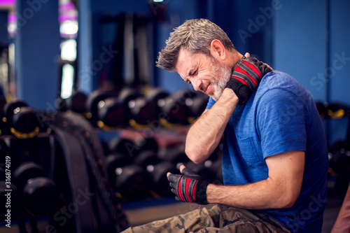 Man feeling strong neck pain while training in the gym. People, fitness and healthcare concept © Aleksej