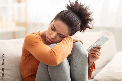 Canvastavla Sad Woman Holding Cellphone Sitting On Couch At Home