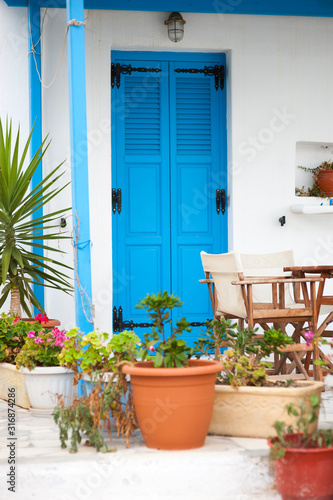 Greek blue door with whitewashed stucco walls framed by Mediterranean potted plants © PeskyMonkey