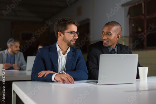 Smiling businessmen using laptop in dark office. Professional multiethnic businessmen working with laptop computer late at night. Working late concept