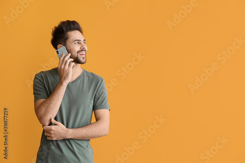 Happy young man talking by mobile phone on color background photo